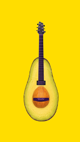Half of avocado in shape of guitar on bright yellow background. Contemporary art. Artistic reinterpretation, playful twist of food and music. Concept of surrealism, pop art, creativity, imagination.