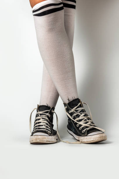 Old blue sneakers hipster style on girl legs in over the knee socks, on a white background