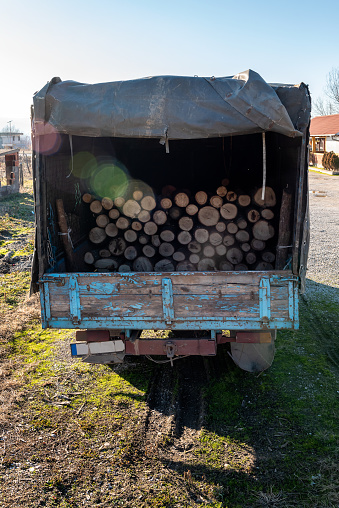 Old and shabby utility truck packed with wood logs for sale use in fire place at home stored on forest woods green biomass energy