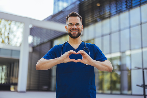 Closeup shot of a medical practitioner making a heart shape with his hands. Cheerful male surgeon touching fingers in shape of heart and holding hands near chest.