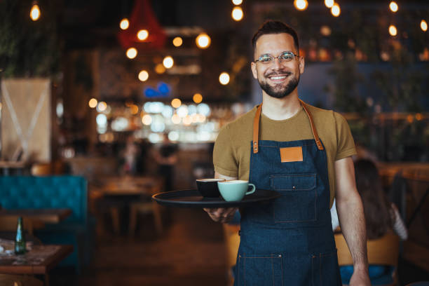 istock Young waiter serving coffee in a cafe and looking at camera. 2149636721