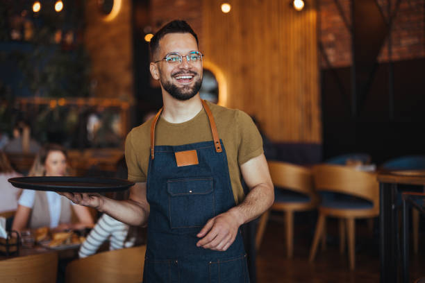 istock Young waiter serving coffee in a cafe and looking at camera. 2149636736