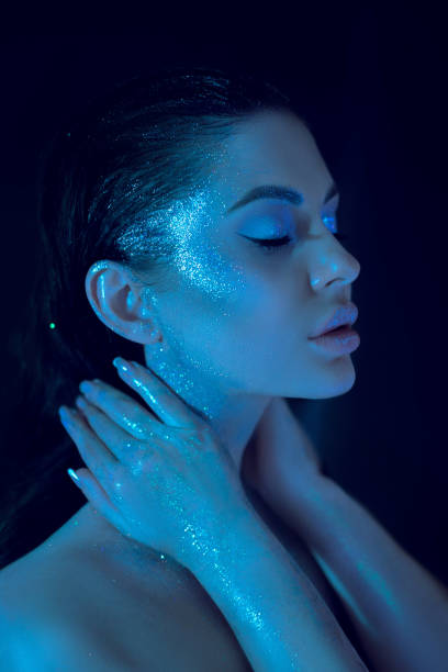 istock Woman with shimmering blue cosmetic makeup, serene pose, face and hand glowing under a soft blue light 2149637108
