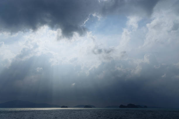 Sunlight filters through dark storm clouds above a tranquil sea, casting rays upon the water