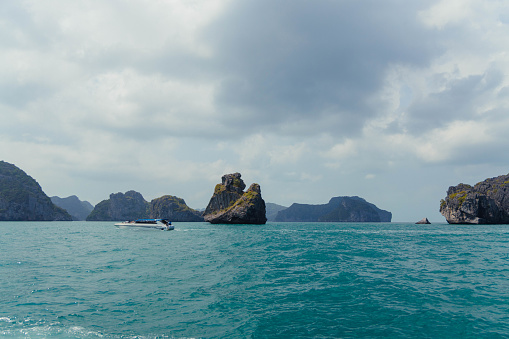 Speedboat sails through calm blue waters near large rock formations under a cloudy sky