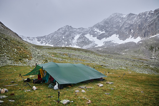 Solitary green tent set up on a rocky terrain against the backdrop of towering snow-capped mountains