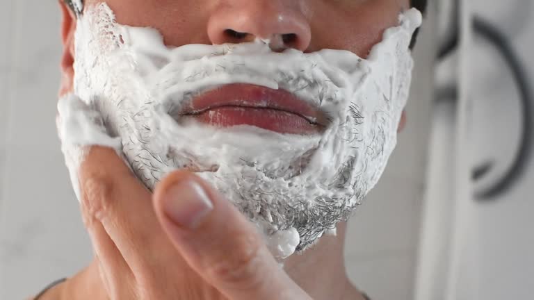 Young guy applying shaving foam. A man shaves his beard, close-up.