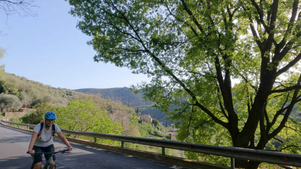 Mature woman e-bikes rural road in forest