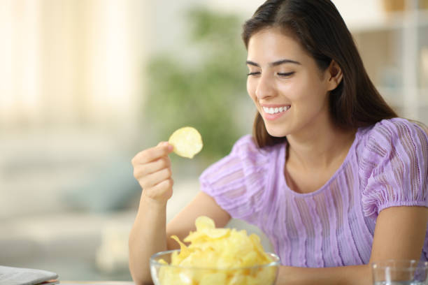 istock Happy woman eating potato chips smiling at home 2149645057
