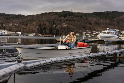 Man in his 30s seated in a boat, surrounded by the tranquility of a Norwegian fjord.