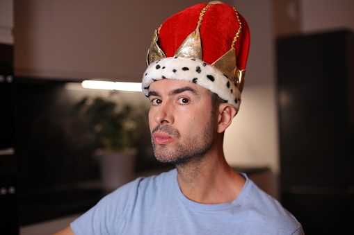 A modern day man in his early forties is pretending to be a king. He wears a comedic baroque velvet hat and poses with pride.