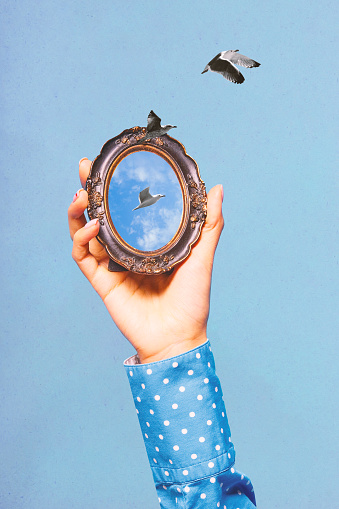 Poster. Contemporary art collage. hand holding mirror with reflection of ocean horizon with flying seagulls against blue background. Concept of inspiration, surrealism, fashionable. Pop art.