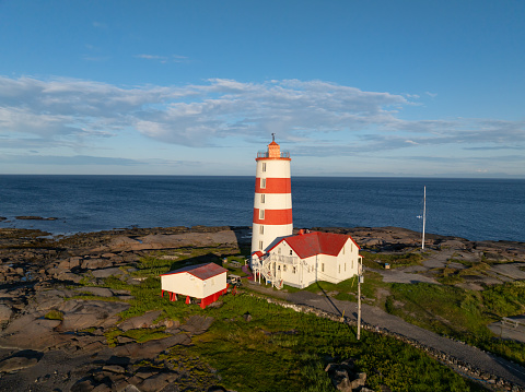 Aerial view of Pointe-des-Monts Lighthouse at sunrise, Cote-Nord, Quebec. The sun is setting over the St. Lawrence river on this day of summer in Cote-Nord, Quebec, Canada.