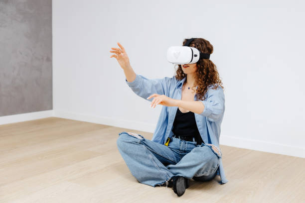 istock Young woman in VR glasses using modern technology creating room design, moving hands in air, sitting in new apartment during renovation. Virtual reality and repair concept. 2149656585