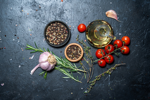Ingredients. Cherry tomatoes, rosemary, thyme, garlic and dry pepper on rough black textured background.