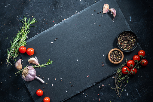 Black slate serving plate, decorated with ingredients: tomatoes, rosemary, garlic and dry pepper.