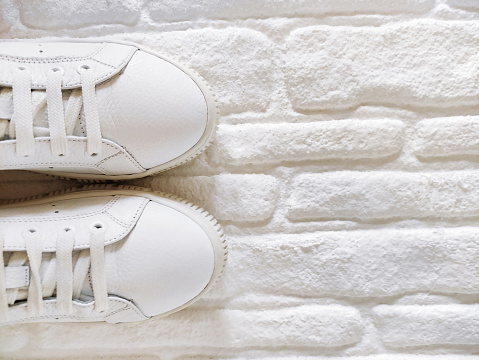 White sports sneakers with laces on  white brick background