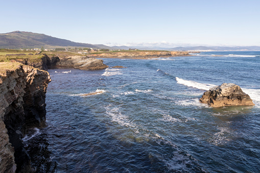 scenic coastline with rocky cliffs, blue ocean waves, and distant mountains under a clear sky
