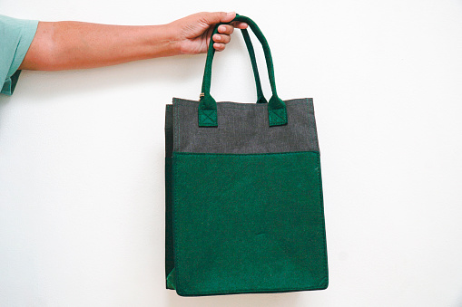 A hand holding a green and gray felt tote bag.