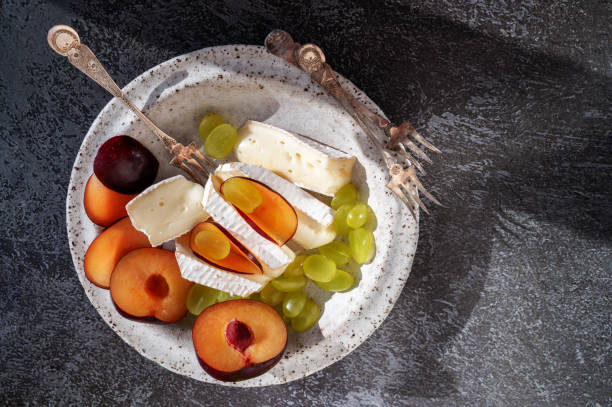 istock Camembert brie cheese with grapes and plums. Camembert and brie, sliced into bite-size pieces. Cheese served on handmade plates. Top view, flat display, hard light 2149662594