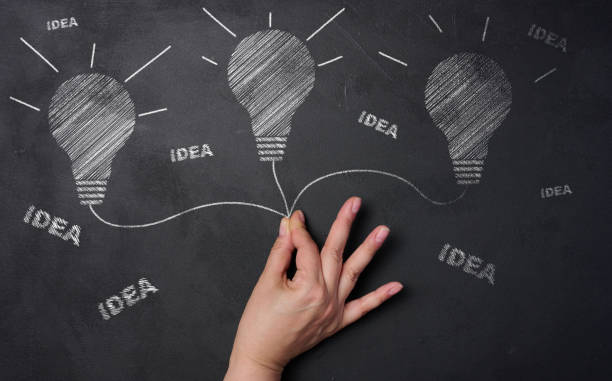Drawn light bulbs with white chalk on a black board and a woman's hand searching for new ideas