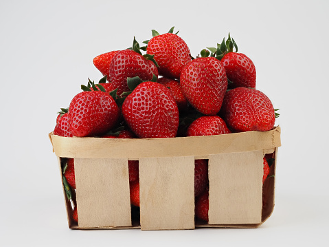 Basket full of luscious ripe red strawberries with stems in close up over a green spring meadow background