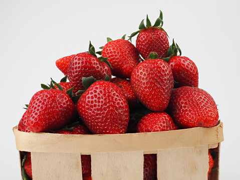 Basket full of luscious ripe red strawberries with stems in close up over a green spring meadow background