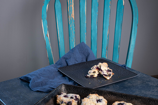 Blueberry biscuit or scone broken in half honey drizzled over. Blue napkin, table and chair.