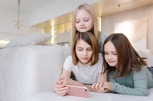 Three girls are laying on couch and looking at a phone. Scene is lighthearted and playful