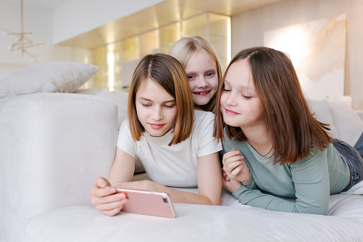 Three girls are laying on couch and looking at phone. They are smiling and seem to be enjoying themselves
