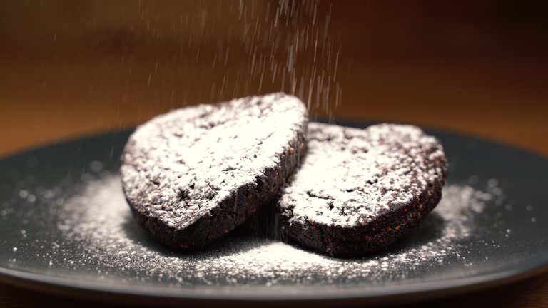 Two chocolate cookies on a black plate with a sprinkle of powdered sugar on top