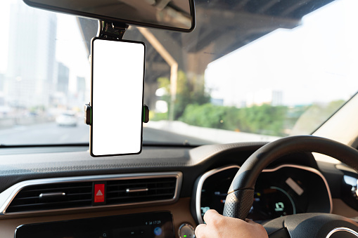 People are driving with an empty front phone holder, clipping path. The phone holder is white and has a red button on it. A car is on the highway with a bridge in the background.