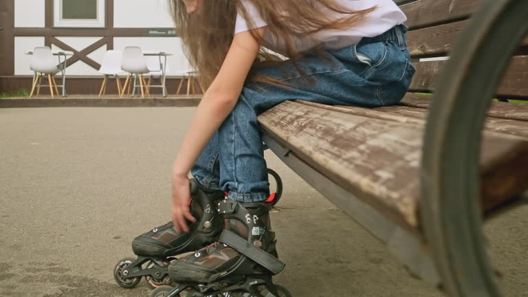little girl to put on roller skates while sitting outdoors on street bench