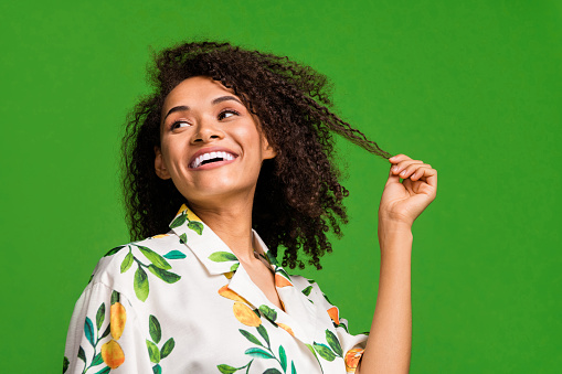 Photo of flirty girly lady wear print shirt smiling holding hair curl looking empty space isolated green color background.