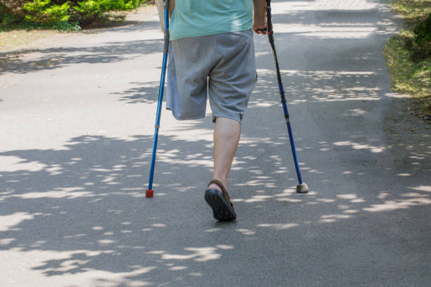 One-legged man with crutches on a walk in summer park