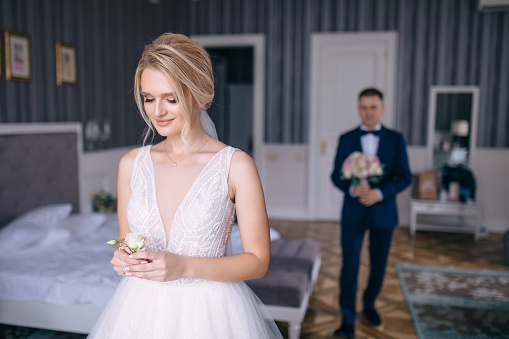 the groom enters the bride's room with a bouquet. Girl holding boutonniere