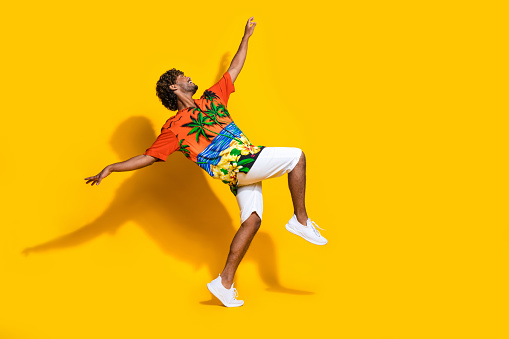 Full size photo of positive man dressed print shirt white shorts dancing look up at offer emty space isolated on yellow color background.