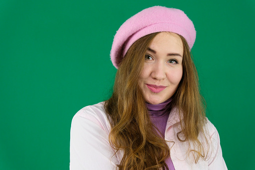 young girl woman with a pink beret on her head France fashion on a green background chromakey. different emotions pink jacket gloves long brown hair. pink winter autumn knitted. gloves on hands
