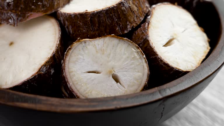 Raw yucca (cassava) sliced root in wooden bowl on a kitchen rustic table close up. Rotation