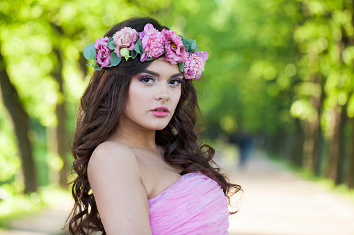 Attractive healthy woman with makeup and long wavy dark brown hairstyle with flowers on head in spring park outdoor