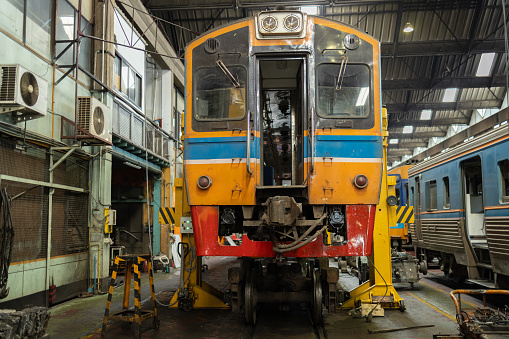 Front view of a colorful train receiving maintenance in a well-equipped railway depot workshop.