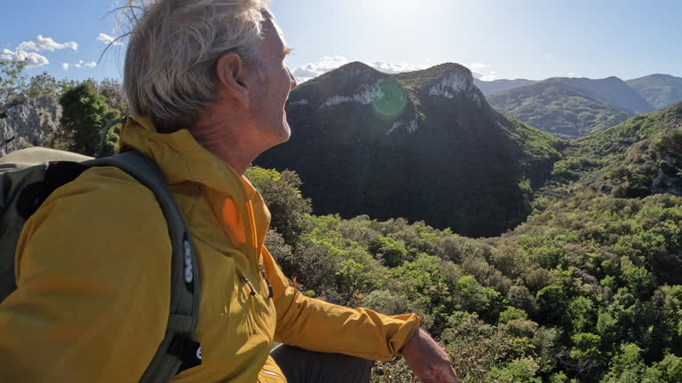 Mature man ascends rock ridge crest, POV persepctive