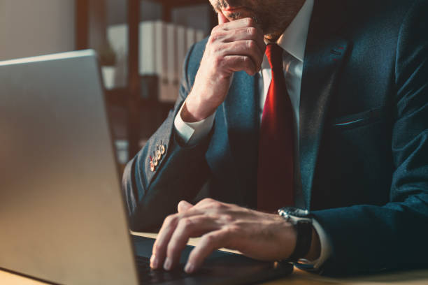 istock Worried businessman working on laptop computer late at night in dark office, thinking with hand on the chin 2149680949