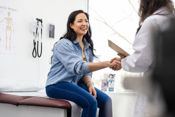 Mid adult female patient shakes hands with her new doctor The mid adult female patient sits on the examination table and shakes hands while she meets her new doctor. primary care stock pictures, royalty-free photos & images