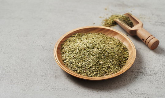close up yerba mate tea leaves in wood bowl and scoop on white table food copy space background