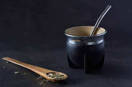 lack mate with bombilla in black background and a wooden spoon with yerba mate. copy space.