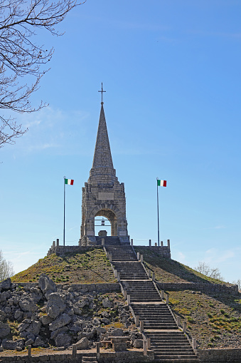 Tonezza, VI, Italy - April 14, 2024: very long  stoned Staircase and Italian flags and the spire of the Monte Cimone ossuary
