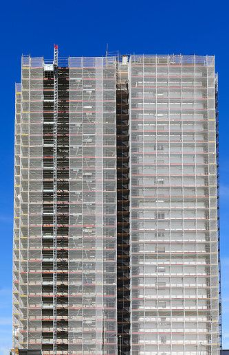 huge scaffolding of the gigantic skyscraper during maintenance to install the thermal insulation for energy saving and blue skye