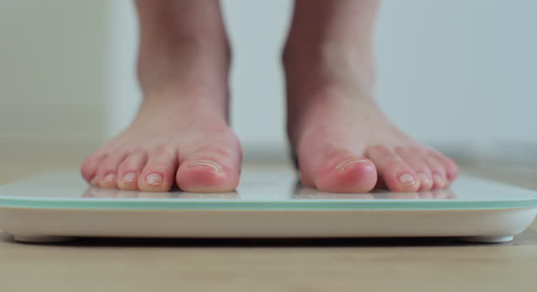 Young woman barefoot legs stepping on floor scales. Woman feet standing weighing scales slimming. Weight lose scales measure weight. Health and wellness.