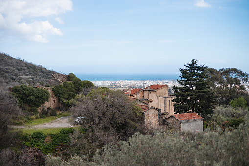 Alassio, Italy - March 28, 2024: Picturesque breathtaking view from the heights of the mountains - the wealth of nature and buildings of medieval architecture in the distance - an abandoned castle